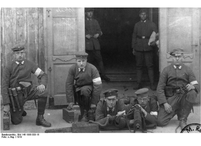 B&W photograph of 7 soldiers of the Freikorps 1918, 2 standing inside a doorway, 3 kneeling and 2 lying on their fronts