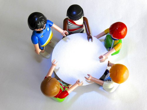 5 Playmobil figures positioned round a white table, photographed from above by Hebi B.from Pixabay https://pixabay.com/photos/playmobil-characters-meeting-451203/