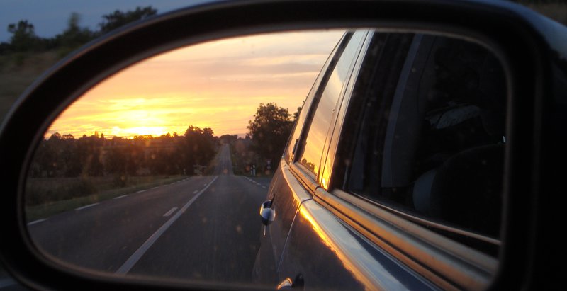 reflection of sunset over road an trees in a car wing mirror